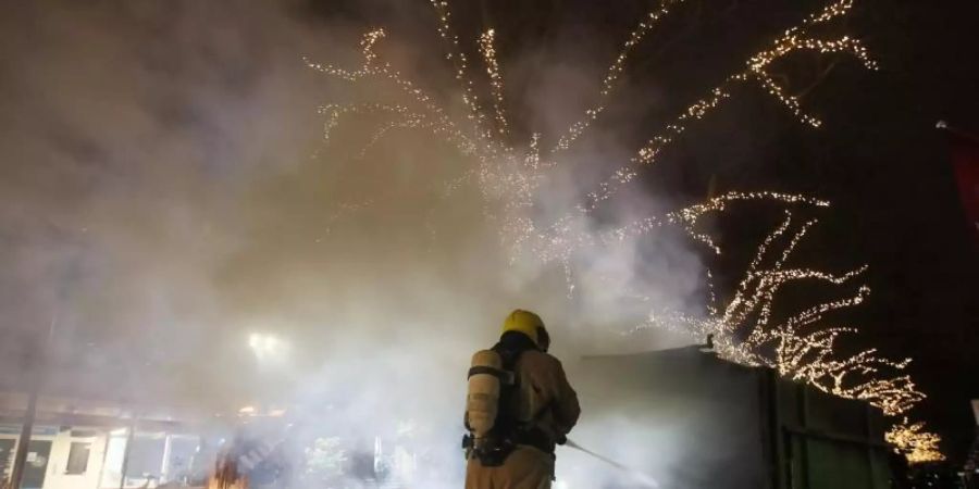 Krawalle in Rotterdam: Ein Feuerwehrmann löscht einen Container, der bei Protesten gegen die landesweite Ausgangssperre in Brand gesetzt wurde. Foto: Peter Dejong/AP/dpa