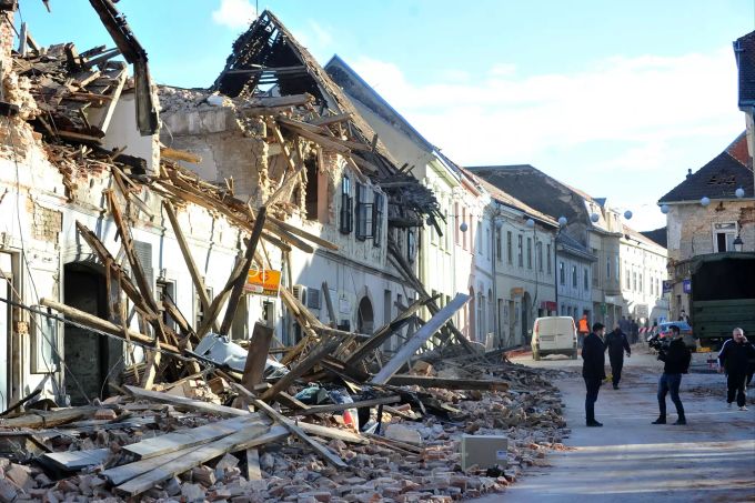 Zwei Passanten machen ein Foto vor den Trümmern eines durch ein Erdbeben eingestürzten Hauses. Ein Erdbeben der Stärke 6,4 hat nach Angaben von Seismologen erneut die kroatische Zentralregion erschüttert. Erdbeben in Kroatien
