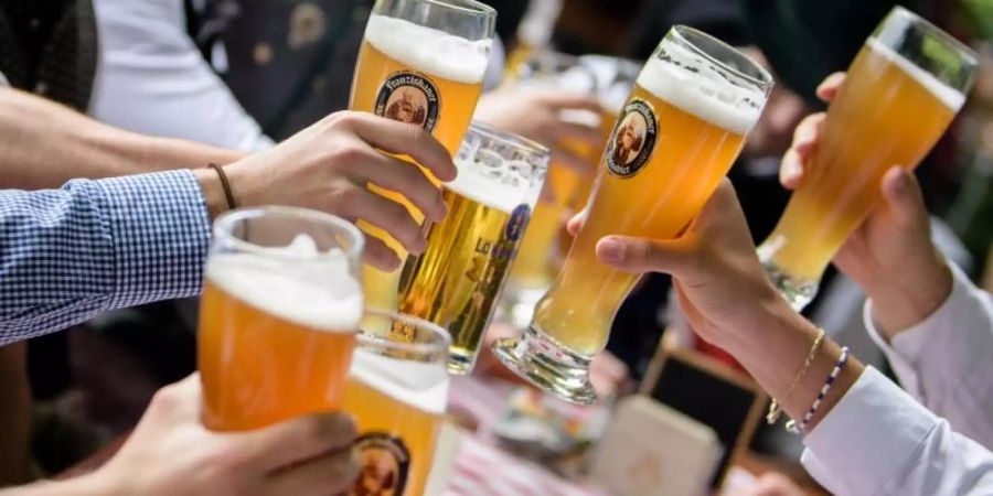 Die Gäste sind zahlreich vorhanden, aber Mitarbeiter in der Gastronomie sind schwer zu finden. Eine Männergruppe stösst im Biergarten eines Wirtshauses an der Isar mit Weissbiergläsern an. Foto: Matthias Balk