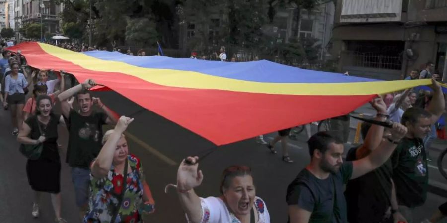 Menschen halten eine rumänische Flagge während einer Demonstration zum Gedenken an ein getötetes 15-jähriges Mädchen in Bukarest. Foto: Vadim Ghirda/AP