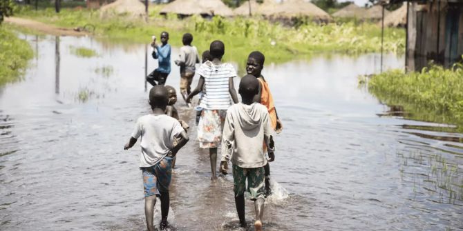 Kinder in Uganda waten auf einer überschwemmten Strasse