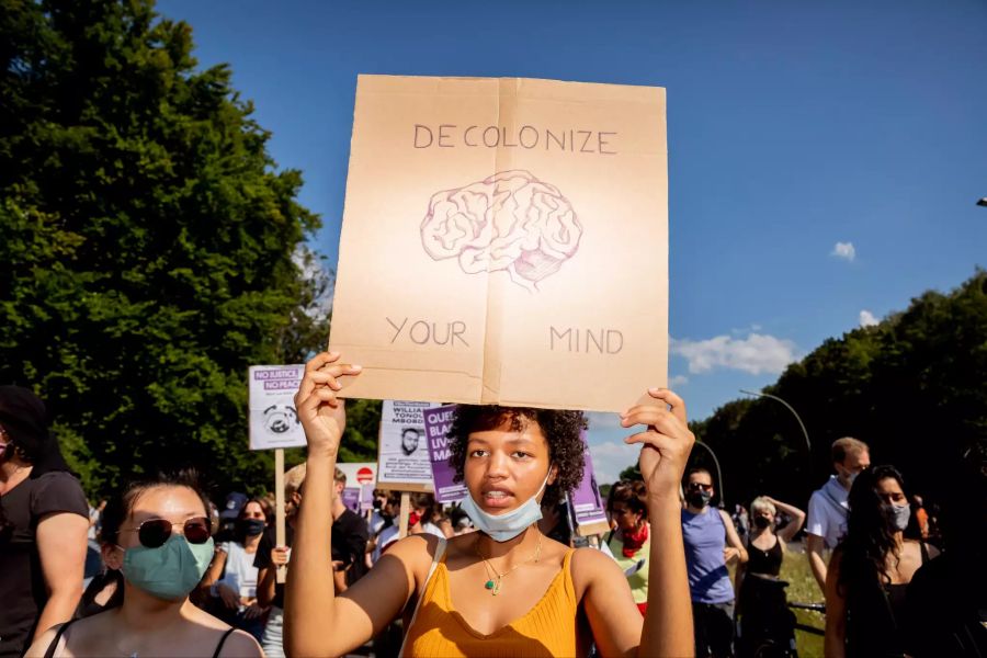 Eine junge Frau hält ein Schild mit der Aufschrift «Decolonize your mind» (Entkolonialisiere deinen Kopf).