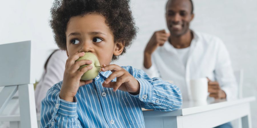 Kind isst Apfel, Vater im Hintergrund