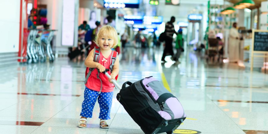 kleinkind am flughafen schiebt eigenen koffer