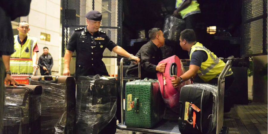 Polizisten tragen Taschen und Koffer zu einem LKW.