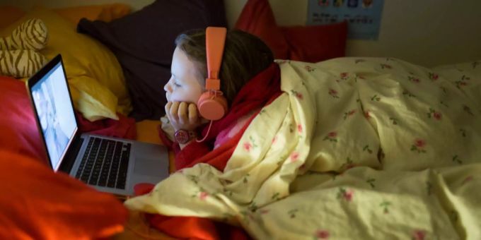 Im Bett liegend schaut ein Mädchen ein Fernsehprogramm über einen Laptop. Im Bett liegend schaut ein Mädchen ein Fernsehprogramm über einen Laptop.