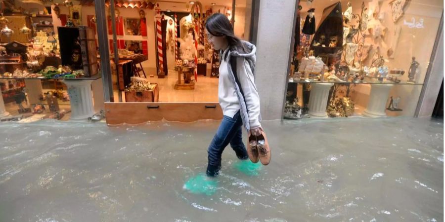 Eine Frau läuft im überschwemmten Venedig vor einem Schaufenster durch.