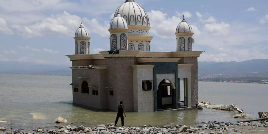 Ein Mann schaut auf eine Moschee, die vollständig von Wasser umgeben ist.