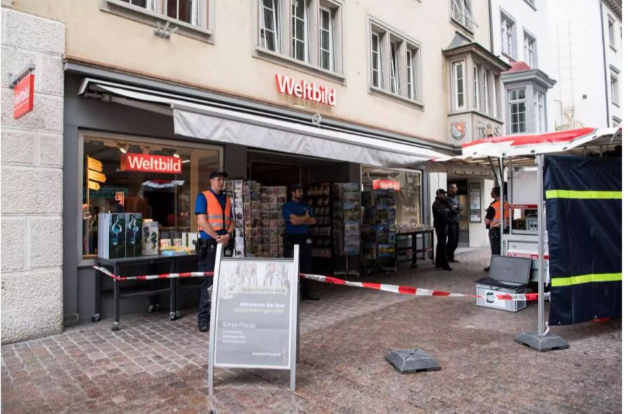 Polizisten stehen vor einer Weltbild-Filiale in Schaffhausen dessen Altstadt abgeriegelt ist, während die Beamten den Motorsägen-Angreifer suchen.