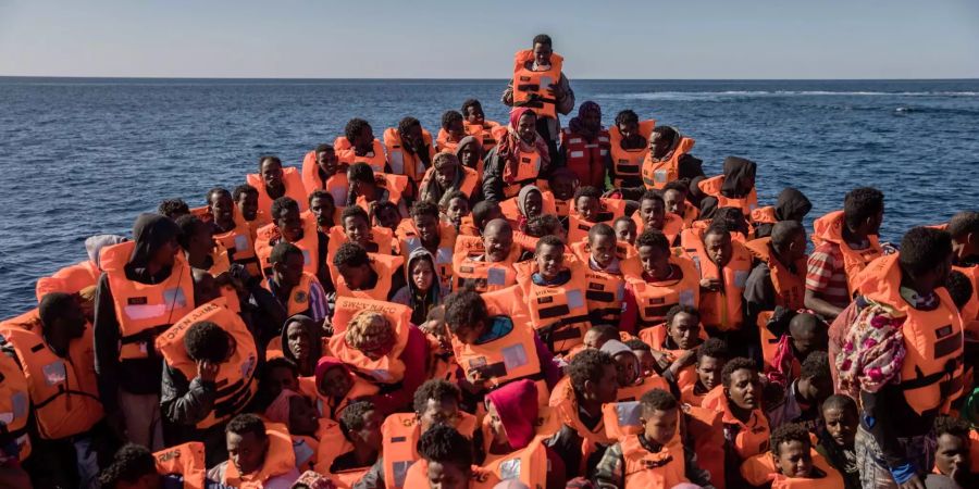 Flüchtlinge in einem Boot warten auf die Ankunft eines Schiffes, dass sie rettet.