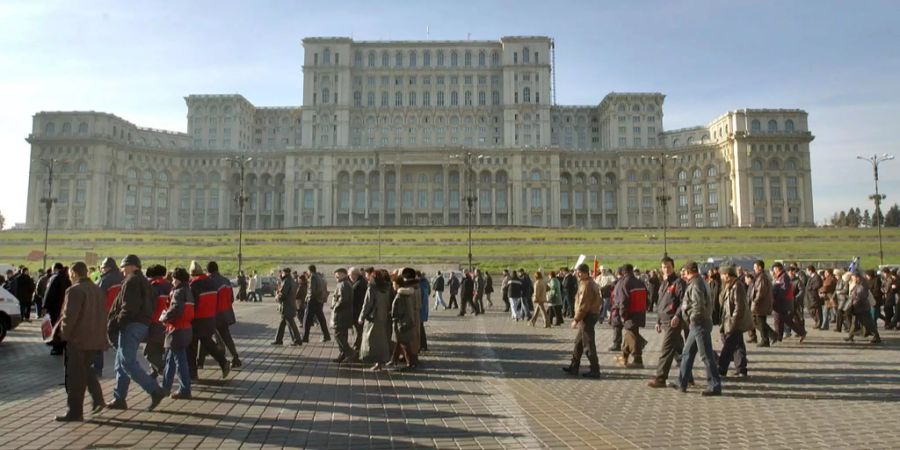 Rumänische Postarbeiter gehen an einem riesigen kommunistischen Ärapalast vorbei, der während der Zeit des ehemaligen Diktators Nicolaie Ceausescu in der Hauptstadt Bukarest gebaut wurde.
