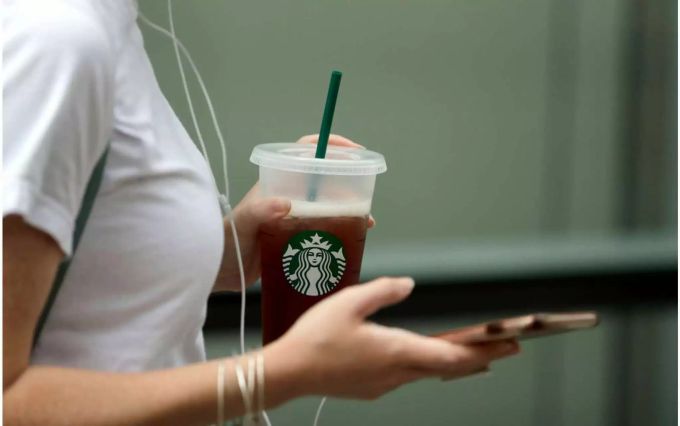 Eine Frau geht mit einem Starbucks Becher umher. Starbucks
