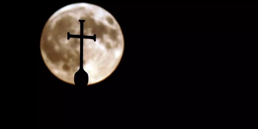 Das Kreuz auf einer Kirche ist vor dem Mond zu sehen.