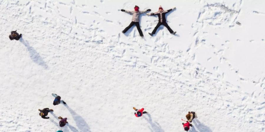 Kinder spielen im Schnee, andere Menschen spazieren beim gefrorenen Lac de Joux vorbei.