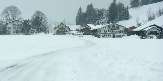 Wegen zahlreicher unter der Schneelast umgekippter Bäume bleibt die Staatsstrasse nach Lenggries und Walchensee gesperrt. : Eine mit Schnee bedeckte Strasse führt ins Dorf Jachenau.
