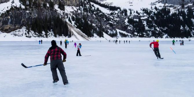Mehrere Personen spielen auf dem gefrorenen Oeschinensee Eishockey.