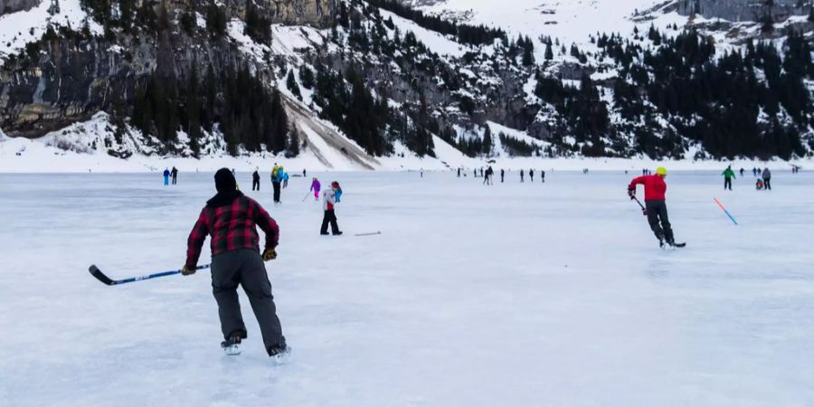 Mehrere Personen spielen auf dem gefrorenen Oeschinensee Eishockey.