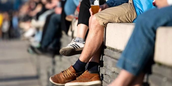 Menschen sitzen auf einer Mauer am Rheinboulevard in Köln und geniessen die Sonne. meteorologie