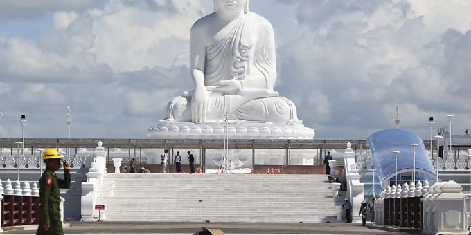 Ein Soldat geht an Frauen vorbei, die unterhalb der Marmorstatue des Maravijaya-Buddha arbeiten. myanmar