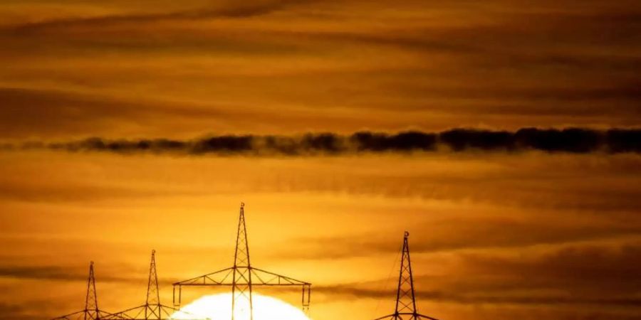 Die Sonne geht hinter Hochspannungsmasten auf (Symbolfoto). Foto: Sebastian Gollnow/dpa
