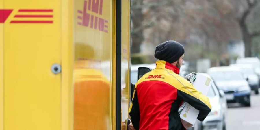 Ein DHL-Paketzusteller verlässt mit mehreren Sendungen sein Fahrzeug. Foto: Jan Woitas/zb/dpa