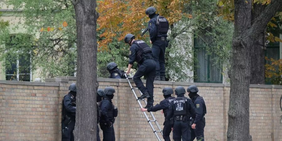 Polizisten mit Schutzhelmen übersteigen eine Mauer in Halle (D).