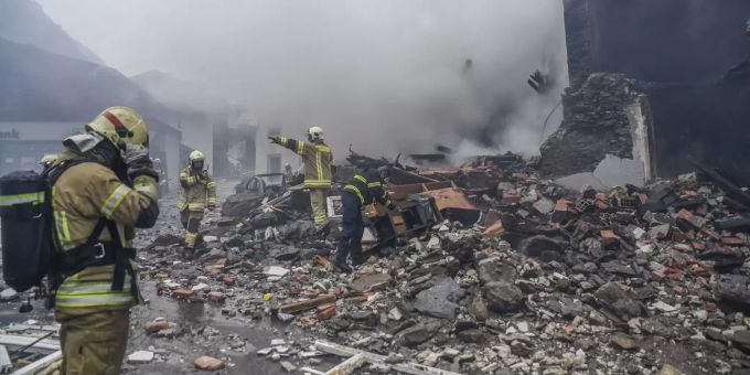 Feuerwehrmänner stehen im Brandschutt eines Gebäudes, während im Hintergrund Rauch aufsteigt. Explosion in Tirol