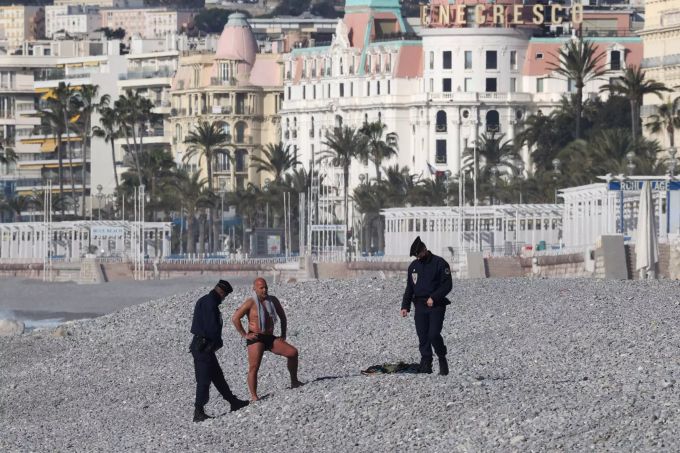 Ein Mann in Badehose wird von zwei französischen Polizisten an einem Strand kontrolliert. Coronavirus - Frankreich