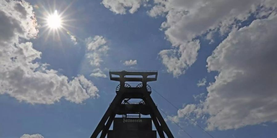 Die Sonne scheint hinter dem Förderturm der Zeche Zollverein in Essen. Foto: Oliver Berg/dpa