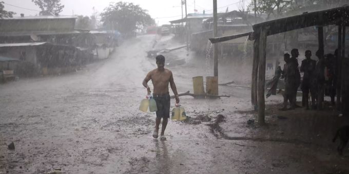 ARCHIV - 31.05.2019, Panama, La Penita: Ein Migrant bringt im strömenden Regen Trinkwasserkanister zu einem Lagerhaus, das im Darien-Regenwald Migranten als Unterkunft dient. Migration durch den Darién-Dschungel