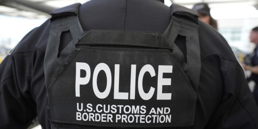 ARCHIV - Ein Beamter der Zoll- und Grenzschutzbehörde beobachtet, wie die damalige US-Heimatschutzministerin Noem durch den San Ysidro Port of Entry geht. Foto: Alex Brandon/AP/dpa