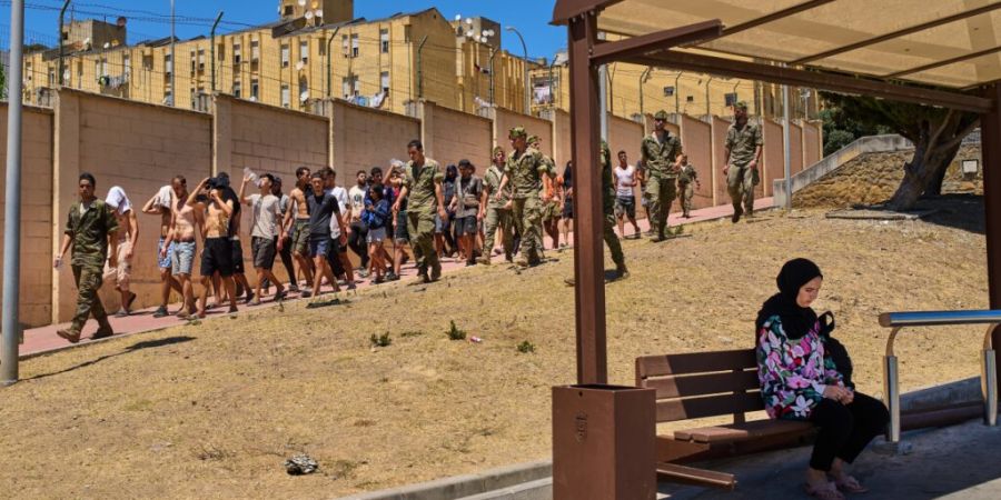 dpatopbilder - Eine Einwohnerin von Ceuta sitzt an einer Bushaltestelle, während Migranten, die nach Spanien eingereist sind, von spanischen Soldaten in Richtung der spanisch-marokkani...