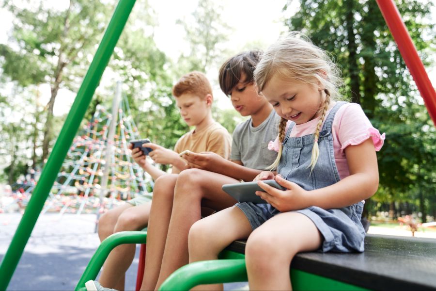 Kinder auf einem Spielplatz schauen auf ihre Handys