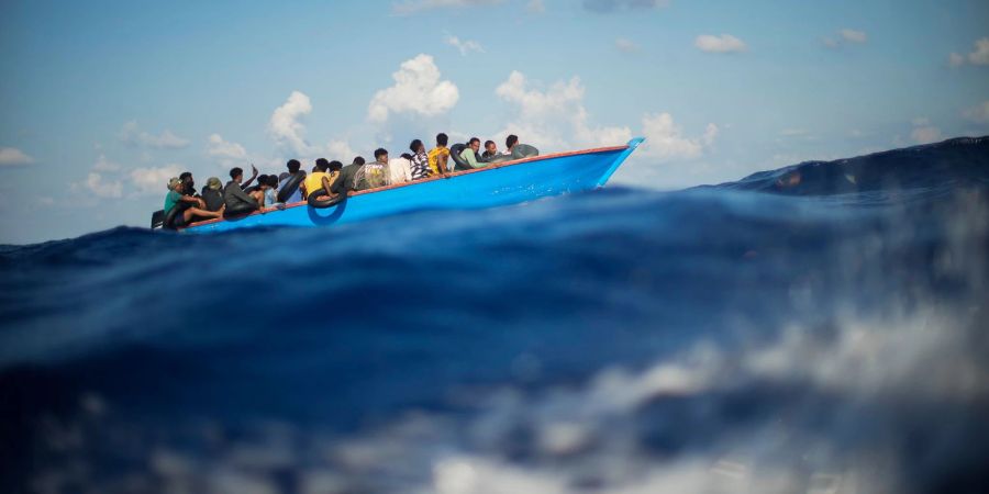 Menschen, die nach Europa wollen, sitzen in einem Holzboot im Mittelmeer. Symbolbild