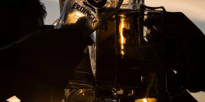 Junge Menschen stossen im Sonnenuntergang in einem Biergarten mit Biergläsern an. Junge Menschen stossen im Sonnenuntergang in einem Biergarten mit Biergläsern an.