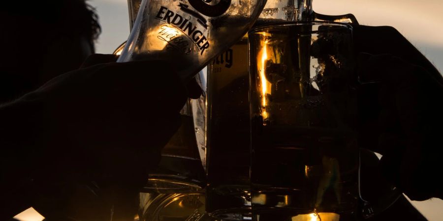 Junge Menschen stossen im Sonnenuntergang in einem Biergarten mit Biergläsern an.