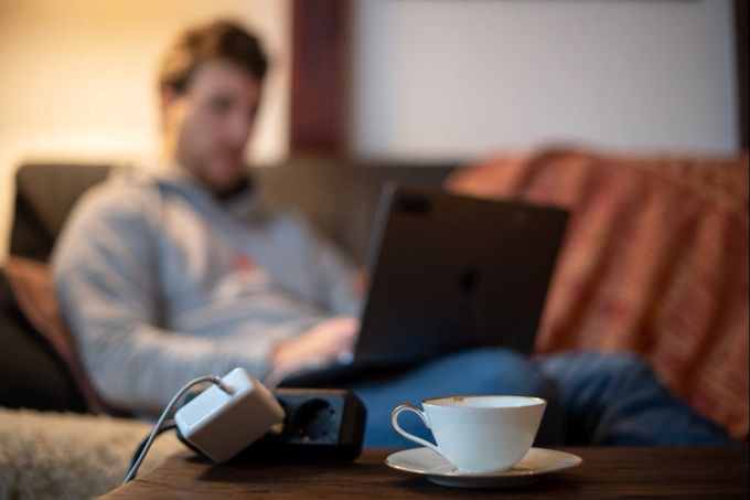 Ob man nun auf dem Sofa arbeitet oder am Schreibtisch: Im Homeoffice bewegt man sich naturgemäss eher wenig. Das lässt gerade Hände und Füsse auskühlen. Teetasse Tisch Mann Laptop Steckdose Sofa
