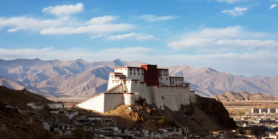 Das Shigatse Kloster in Tibet vor Bergkette und blauem Himmel.