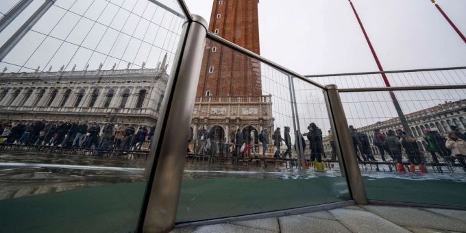 Touristen gehen auf Laufstegen über den überschwemmten Markusplatz. Venedig