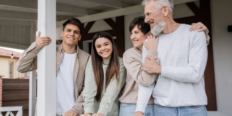 familie strahlt glücklich in die kamera, weisse veranda, middle age, teenager