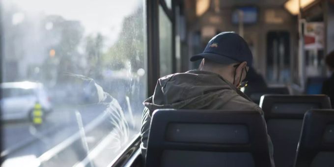 Ein Mann mit Hut, Brille und Maske sitzt in einem Tram in Zürich. Zürich