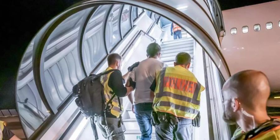 Das Archivfoto aus dem Jahr 2019 zeigt Polizeibeamte, die einen Afghanen bei einer Abschiebung auf dem Flughafen Leipzig-Halle in ein Charterflugzeug begleiten. Foto: Michael Kappeler/dpa