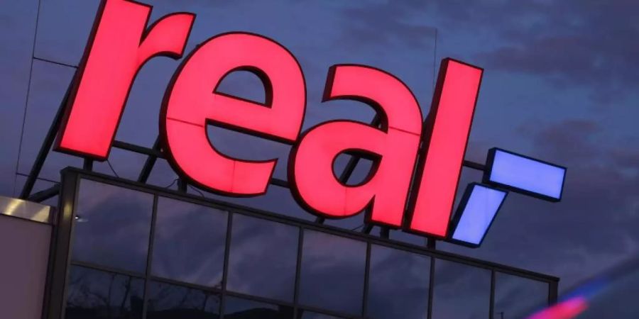 Das Logo leuchtet am Morgen auf dem Dach eines Real Supermarktes. Foto: Oliver Berg/dpa/Archiv
