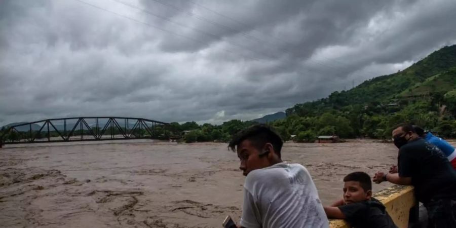 Menschen stehen auf einer Brücke und beobachten wie der Fluss Chamalecon in Honduras über die Ufer tritt. Foto: Seth Sidney Berry/SOPA Images via ZUMA Wire/dpa