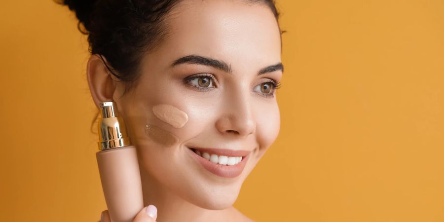 Frau mit zwei Make-Up Streifen auf der Wange hält Foundation Tube in der Hand.