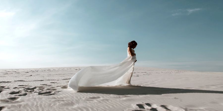 Frau in langem weissen wehenden Kleid steht unter blauem Himmel in der weissen Wüste.