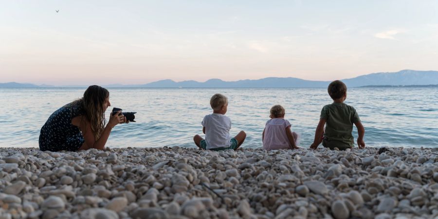 Frau fotografiert Kinder am Strand.