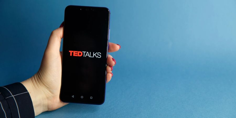 Eine Hand hält ein Smartphone, auf dem das Logo von TED zu sehen ist.