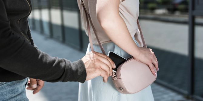 Ein Mann stiehlt einer Frau von hinten ein Handy aus der Handtasche.