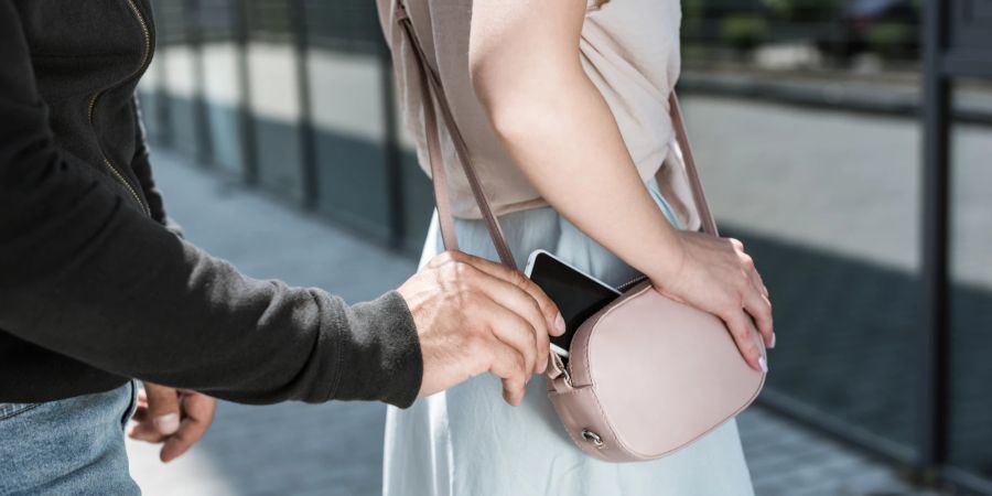 Ein Mann stiehlt einer Frau von hinten ein Handy aus der Handtasche.